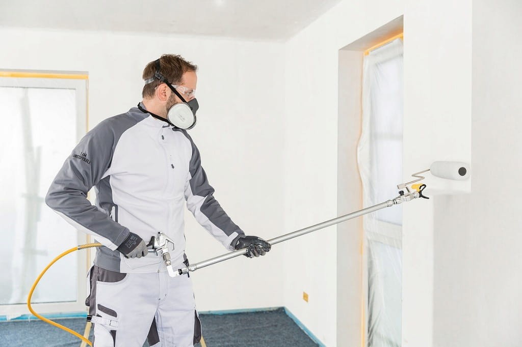Malarz w kombinezonie malujący ścianę agregatem Wagner PowerPainter 90