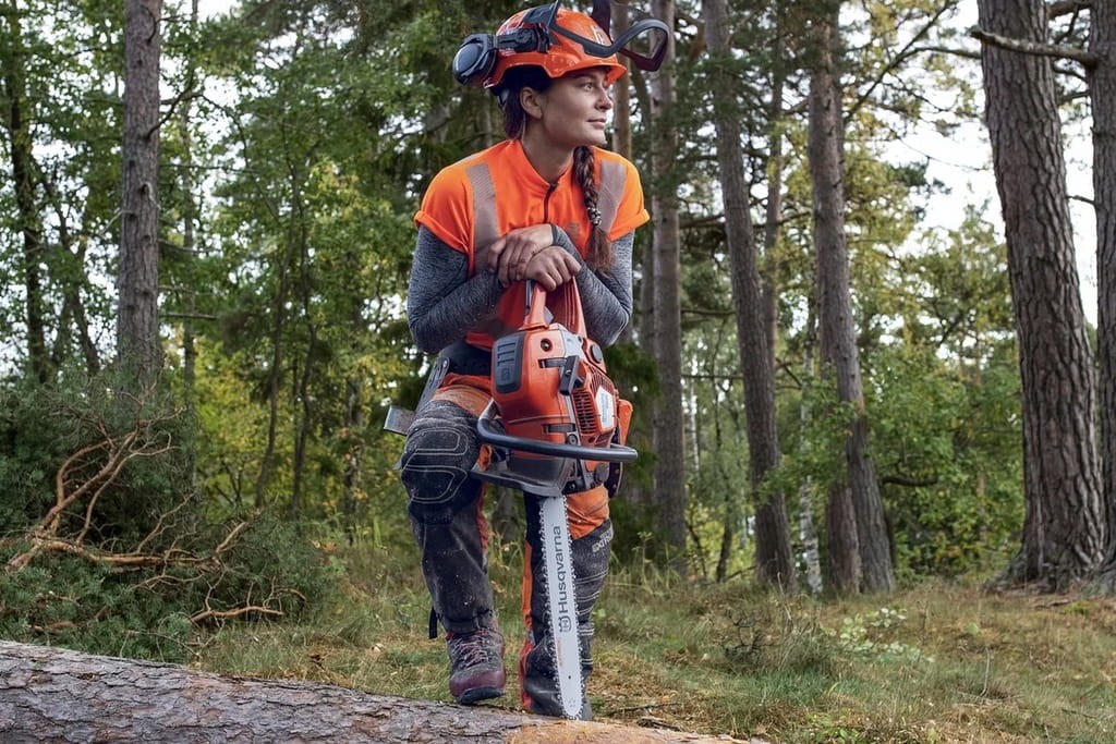 Profesjonalny pilarz przenoszący pilarkę Husqvarna 550 XP w lesie