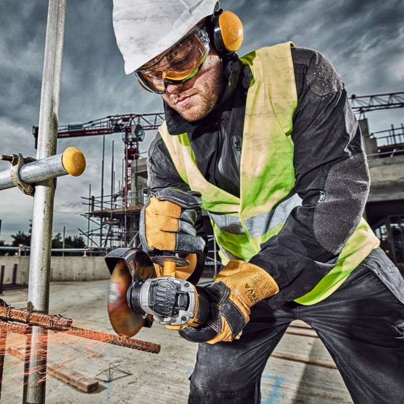 Operator w kasku tnący stal szlifierką DeWalt DCG406 na budowie